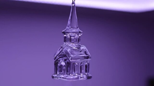 Close up of a small glass church ornament hanging against a purple background.