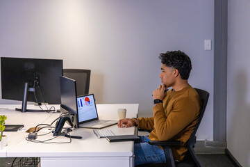 Asian adult man sitting at white office desk reviewing laptop charts and graphs, copy space © wavebreak3