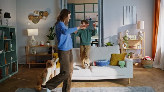 Playful mother son dancing having fun in home living room. Funny boy jumping