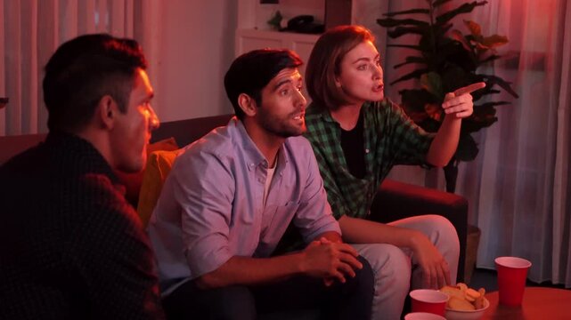 Family and colleague sitting at dark living room with red filter while cheering football team together. Caucasian people enjoy watching tv and giving high five to celebrate winning team. Convocation.