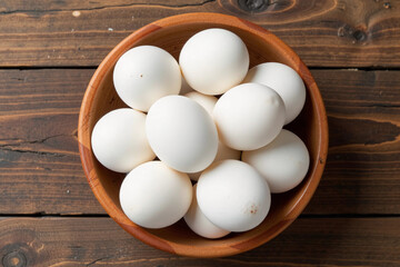 Top view of fresh white chicken eggs in a wooden bowl on a rustic table.