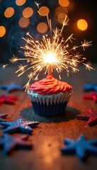 Fototapeta premium Patriotic cupcake with red frosting and a lit sparkler sits on a rustic wooden table. Red and blue glitter stars surround the festive dessert, creating a warm holiday glow.