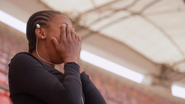black woman in stadium covering face frames show spectator, student, supporter, parent roles, braided hair with earbuds, candid profile and threequarter shots, hands covering face then steadying