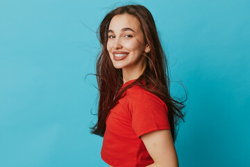 Young woman smiling and posing in red t shirt with long hair against blue background for portrait...