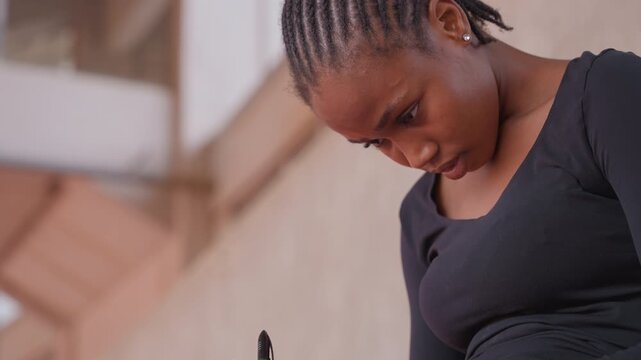 closeup black woman writing in notebook, braided hair and concentrated expression, pen on page, quiet stadium backdrop, intimate study moment captured with natural light and tension of concentration