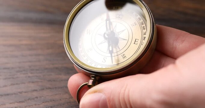 Woman opening compass at wooden table, closeup
