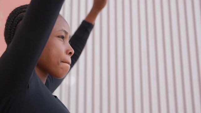 Young black dancer rehearses controlled movements against textured wall. Young black female dancer with braided hair performs precise arm movements during urban dance practice session