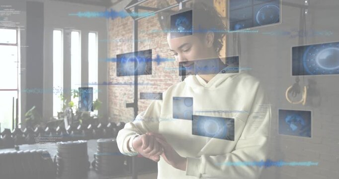 Woman raising wrist and tapping tracker in gym while holographic panels showing workout charts