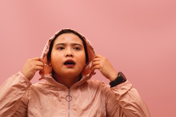 Young Asian female athlete putting on her hoodie hood while preparing for an outdoor or indoor run. © Aulia