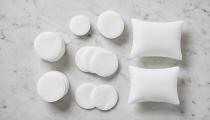 An assortment of round white cotton pads and soft pillows arranged neatly on a textured marble surface