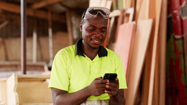 Local African male carpenter using smartphone in his workshop