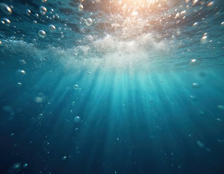 Underwater view of sunlit ocean surface with rising air bubbles and light rays filtering down. Blue water texture with waves and white foam, clear aquatic environment.