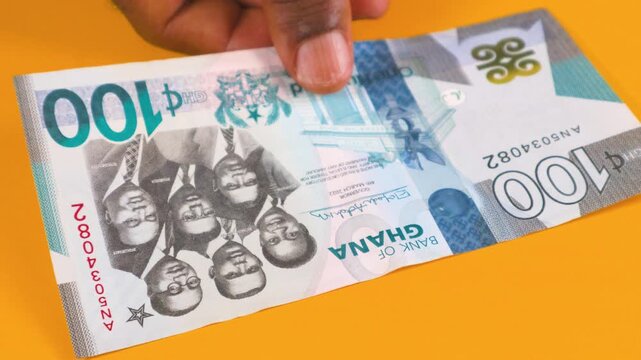A hand displays the various denominations of Ghana Cedi banknotes on an orange surface. The video features the full range from GH₵200 to GH₵1, showing the unique designs and colors of each note.