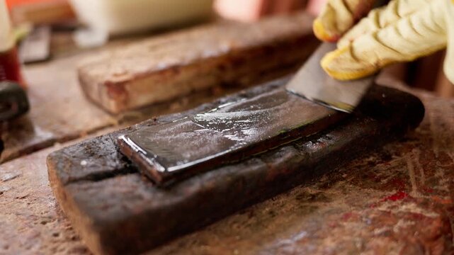 African carpenter, wearing safety gloves, sharpens a blade with a traditional sharpening stone on a rustic wooden workbench in his workshop, closeup