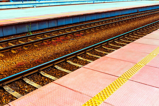 Tactile paving beside parallel train tracks stretching into the distance. Railroad tracks running parallel, separating the main platform from the adjacent raised structure
