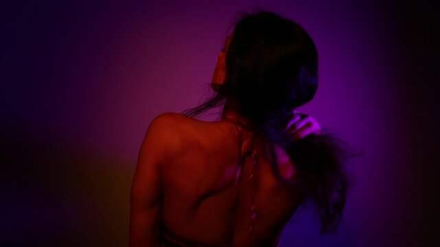 Beauty dancer woman shaking her long hair dancing in a dark studio colorful glows in fantasy club neon with red blue purple lights. Magic blending with sexy body girl. Art creative expression video