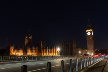 Fototapeta premium Elizabeth Tower and the Palace of Westminster illuminated at night beside a city road. A red double decker bus travels along the bridge under street lighting.