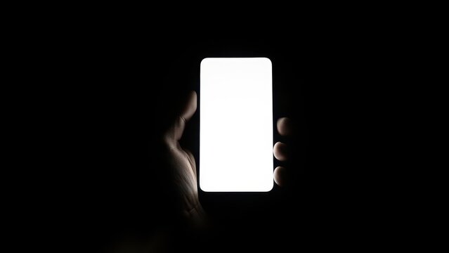 Hand holding smartphone with blank white screen in dark environment, minimalist shot