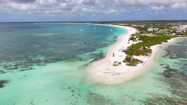Drone view, Princess Diana Beach in Antigua featuring pristine white sandbar, turquoise Caribbean waters, kite surfers, anchored sailboats, and a lush tropical shoreline under dramatic clouds