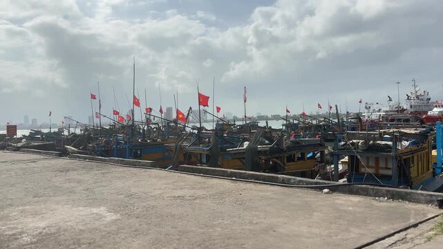 Large fishing fleet docked side by side at Son Tra Marina in Da Nang with red flags raised above decks while cloudy sky hangs over busy harbor scene near city coastline.