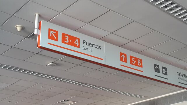 Bilingual directional sign hanging from the ceiling of a modern airport terminal indicating gates, elevators, and the vip lounge