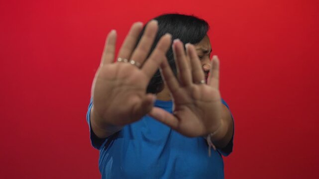 Woman in blue shirt grimaces urgently and extends palms forward in studio; aversion refusal caution barrier.