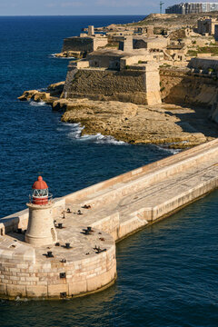 Faro de c&uacute;pula roja en el rompeolas de La Valeta con Fort Ricasoli al fondo. Arquitectura hist&oacute;rica de defensa militar y navegaci&oacute;n en el Mar Mediterr&aacute;neo.