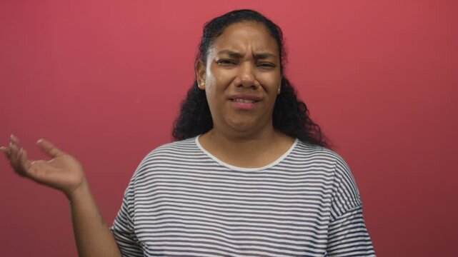 African american woman shrugs hand palm up in studio wearing striped shirt as she frowns and gazes aside; uncertainty.