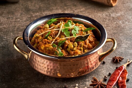 Traditional Indian curry cooking in copper pot with fresh herbs and spices on rustic table