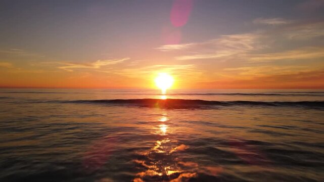 A beautiful golden sunset casts a warm glow over the vast ocean with gentle