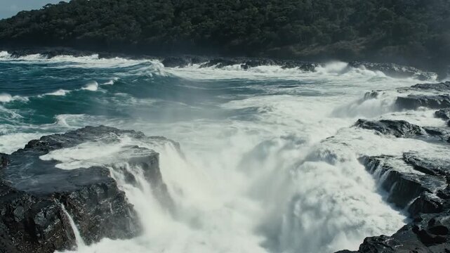 Powerful ocean waves crash against rugged dark s along a wild coastline.