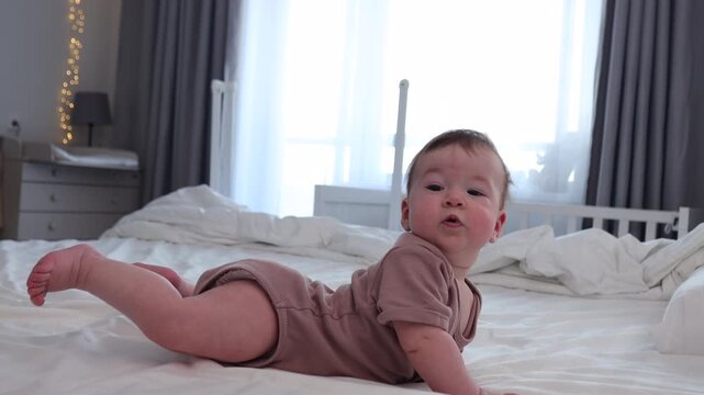 The baby is awake and playing on his parents' bed. He's content, happy, smiling and cooing. He's wearing cute baby clothes.