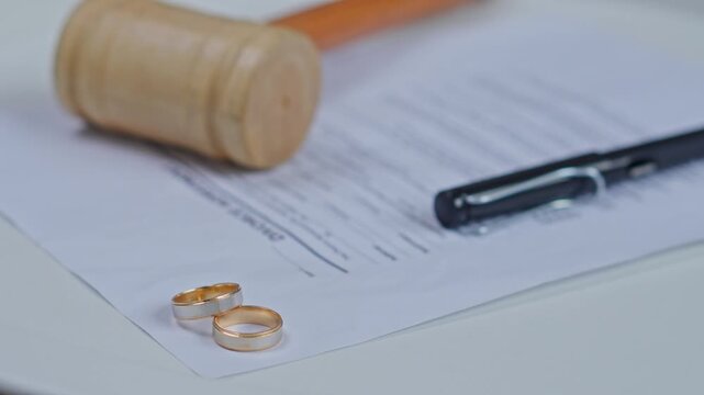 Two gold wedding rings on divorce decree papers with a wooden judge gavel and pen
