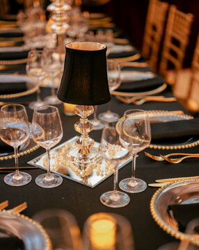 An exquisite dining table setup featuring elegant black and gold elements, a chic lamp centerpiece, and sparkling glassware, perfect for a formal event or dinner party.