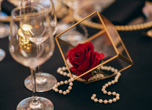 A sophisticated arrangement featuring a single red rose and gold beads in a glass container exemplifies luxury, romance and elegance, perfect for upscale decor and special events.