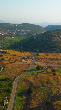 Vertical video. Gelemis, Turkey. Ancient city gate with modern road and Hurmalik Hamami thermal baths at Tepecik, Patara archaeological site in summer morning. Aerial View. Rich colors