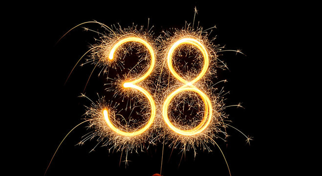 Bright yellow sparkler forming the number 38 against a dark background
