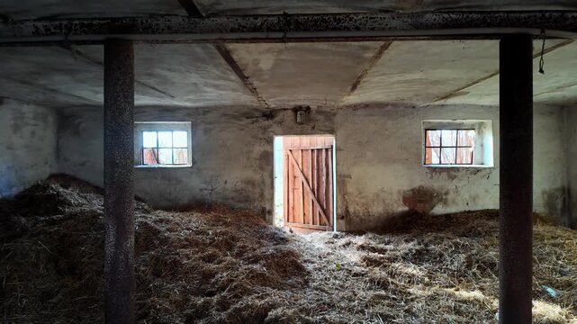Interior of an old stone barn filled with dry hay, open wooden door and small windows in a rustic farm building, traditional agricultural storage, rural architecture and stable.