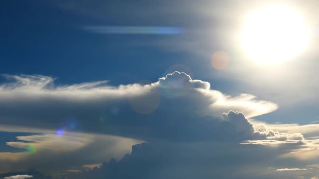 Bright sun shines through a dynamic blue sky with f white clouds