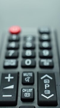 Vertical close-up starts focused on the top of a TV remote, then pulls back to reveal the full remote turning softly out of focus with bokeh, highlighting controls and keypad.