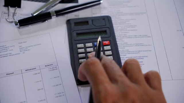 Top view of a calculator on financial paperwork with a hand holding a pen doing budget calculation