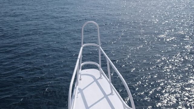View from the bow of a boat over shimmering ocean water, highlighting the railing and deck under bright sunlight, evoking a tranquil maritime scene