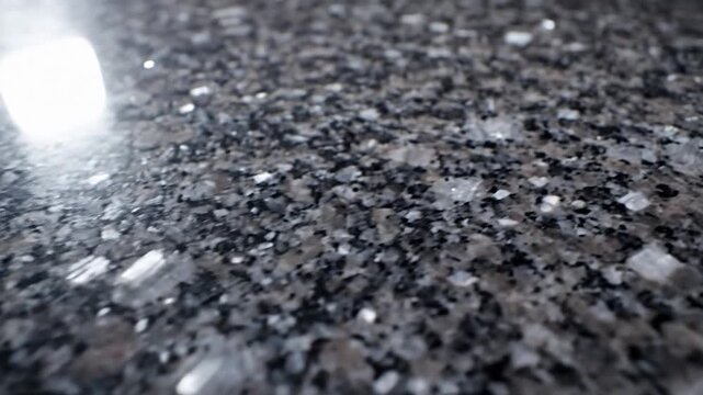 Close-up view of a dark speckled granite surface with a bright reflection