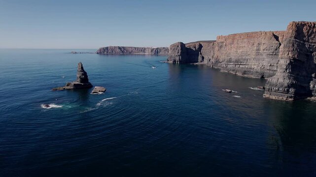 Sea stack rising from Atlantic Ocean beside towering stratified fal&eacute;sias of Vila Nova de Mil Fontes Odemira Alentejo Portugal showing marine erosion platform and sedimentary cliff sequence, drone shot