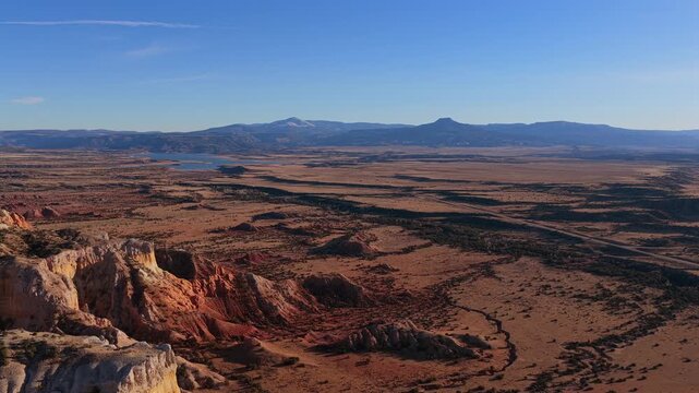 A sweeping drone flight reveals the distinct flat-topped silhouette of Cerro Pedernal in the distance. This 4K vista features the eroded sandstone layers and vast horizon of the Southwest.