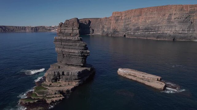 Stratified sandstone sea stack rising from Atlantic water below fal&eacute;sias of Vila Nova de Mil Fontes Odemira Alentejo Portugal showing sediment layer and marine erosion texture as drone pushes forward