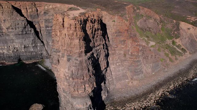Massive sedimentary cliff with visible horizontal bedding, tectonic fracture and marine abrasion base along Atlantic coast of Vila Nova de Mil Fontes Odemira Alentejo Portugal, drone orbiting.