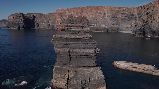 Massive sedimentary sea stack shaped by marine abrasion standing offshore below vertically stratified fal&eacute;sia along Atlantic coastline of Vila Nova de Mil Fontes Odemira Alentejo Portugal, drone orbit