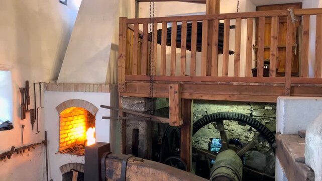 Historic water powered forge with wooden bellows driving air into a blazing furnace. Traditional ironworks machinery in motion, combining fire, airflow and mechanical power in authentic workshop inter