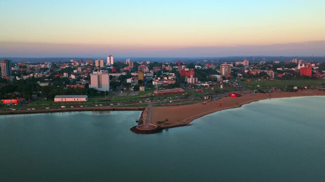 Wide drone panorama of San Jos&eacute; Beach, pier, and city skyline along Paran&aacute; River at sunset in Encarnaci&oacute;n, Paraguay.